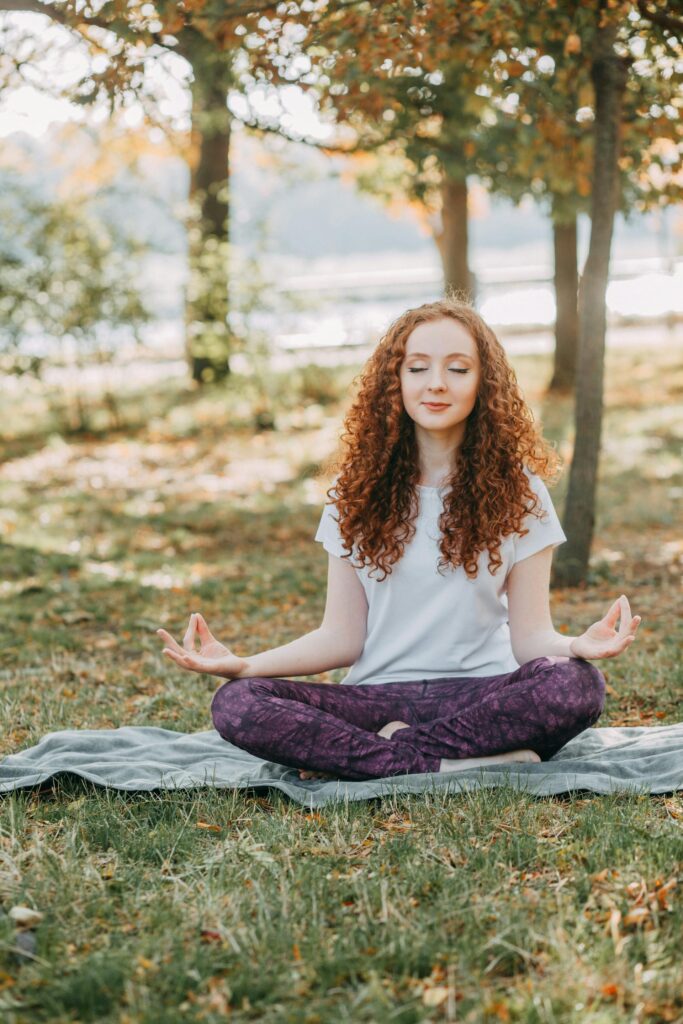 A woman sitting cross-legged and meditating under the trees