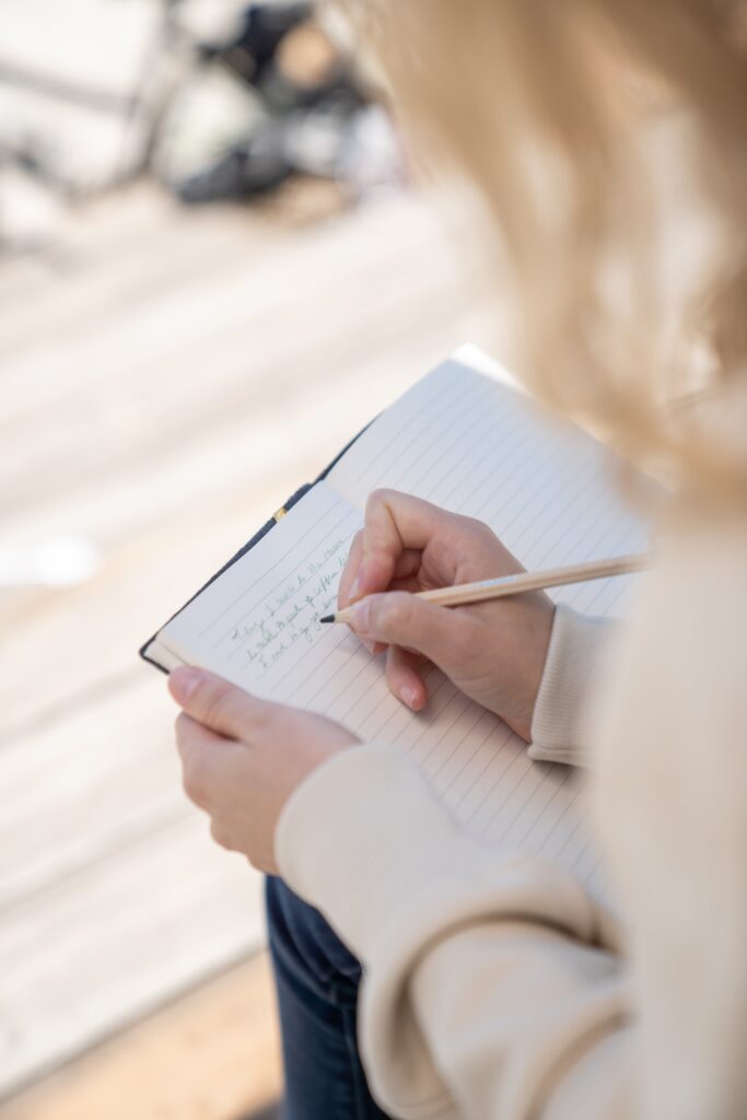 An image taken behind a woman over her shoulder of her writing in a notebook